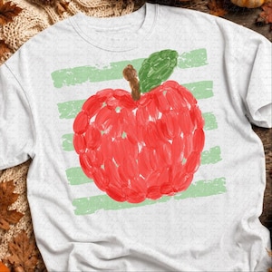 Peut inclure: Un t-shirt blanc à manches courtes orné d'un motif central représentant une pomme rouge avec une tige brune et une feuille verte. La pomme est superposée sur un fond de rayures horizontales vert clair, créant un aspect peint et texturé.