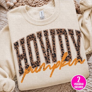 May include: A cream-colored crewneck sweatshirt featuring the word HOWDY in large, block-style letters with a brown and black leopard print pattern. Below the word HOWDY, the word pumpkin is printed in a distressed, textured orange script font.