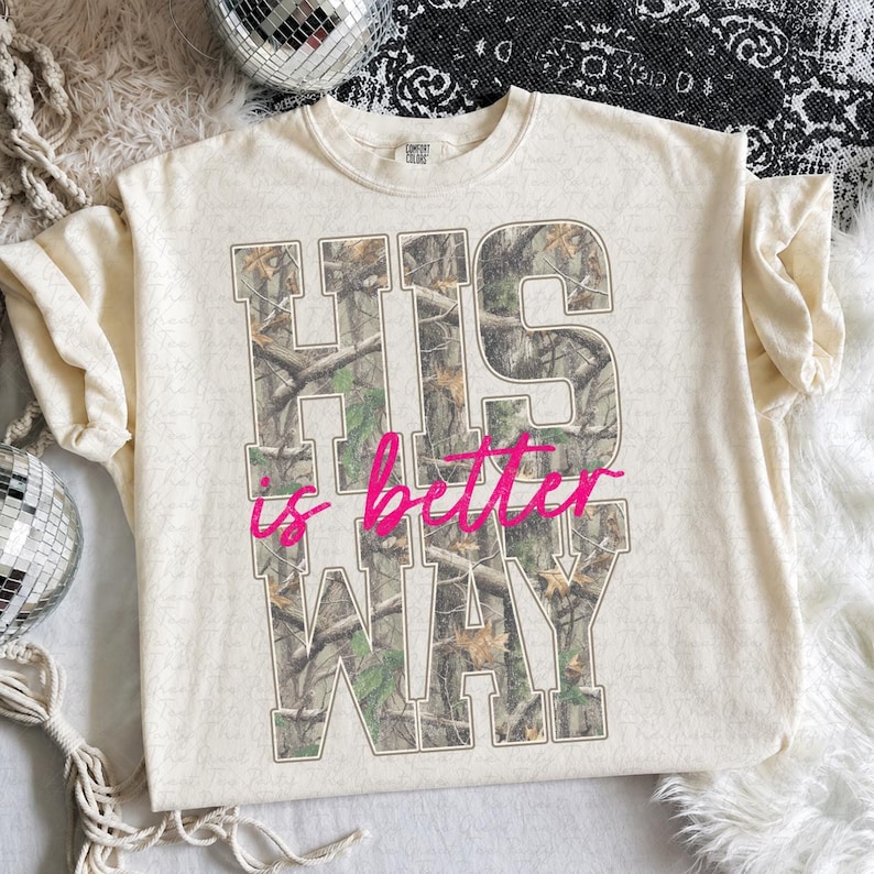 K&ouml;nnte beinhalten: Ein cremefarbenes Kurzarm-T-Shirt mit gro&szlig;en Blockbuchstaben, die HIS WAY mit einem Wald-Tarnmuster-F&uuml;llung zeigen. Die W&ouml;rter is better sind in einer leuchtend pinkfarbenen Schreibschrift &uuml;ber die Mitte des Designs gedruckt.