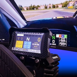 Op de afbeelding: Een close-up van een racesimulatoropstelling met een Fanatec-stuurwiel en displayschermen. De schermen tonen racegegevens, waaronder rondetijden en versnellingsinformatie. De achtergrond is een wazige afbeelding van een racebaan.