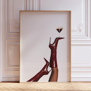 Puede incluir: Impresión enmarcada que presenta un par de botas de tacón alto burdeos con una copa de martini equilibrada en un pie. Las botas son brillantes y llegan hasta los muslos. La copa de martini contiene un líquido oscuro.