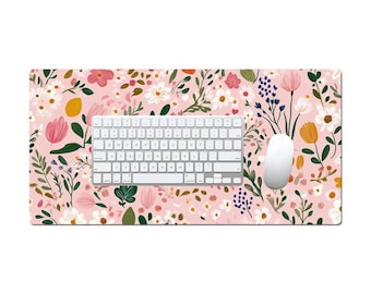 Könnte beinhalten: Eine florale Schreibtischunterlage mit einer weißen Tastatur und Maus. Die Unterlage hat einen rosa Hintergrund mit einem Muster aus Blumen in verschiedenen Farben, darunter Rosa, Weiß, Gelb und Grün. Die Tastatur ist zentriert.