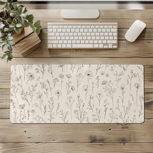 May include: A rectangular desk mat with a cream background and a delicate floral pattern in dark gray. The design features various sketched flowers and foliage, creating a botanical theme. The mat is placed on a wooden desk.
