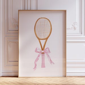 May include: Watercolor illustration of a tennis racket with a light brown wooden frame and a pink bow tied around the handle. The racket's strings are a light beige color. The bow has long, flowing ribbons.