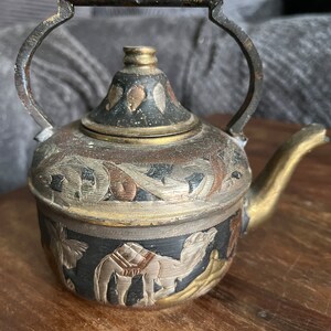 Peut inclure: Une petite théière en laiton ornée avec une poignée en cuivre. La théière est décorée de sculptures complexes de chameaux et d'autres motifs en or, argent et noir.