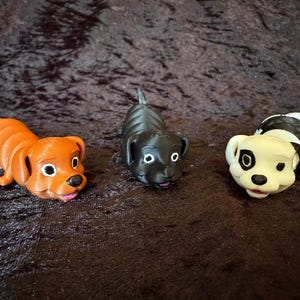 May include: Three toy dachshund dogs in orange, black, and black and white. The orange dog is segmented, the black dog is solid, and the black and white dog has a striped body. All have pink tongues.