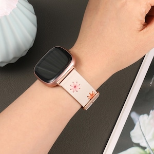 Puede incluir: Una correa de reloj inteligente blanca con un patr&oacute;n floral. La correa est&aacute; hecha de un material suave y flexible y tiene una hebilla de oro rosa. La correa es compatible con la mayor&iacute;a de los relojes inteligentes.