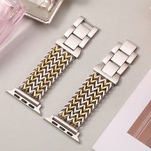 May include: Two silver and gold Apple Watch bands with a woven design. The bands have a silver clasp and are made of metal.
