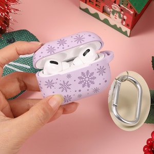 May include: Purple Airpods case with a snowflake design. The case is open and shows the white Airpods inside. A silver carabiner clip is attached to the case.