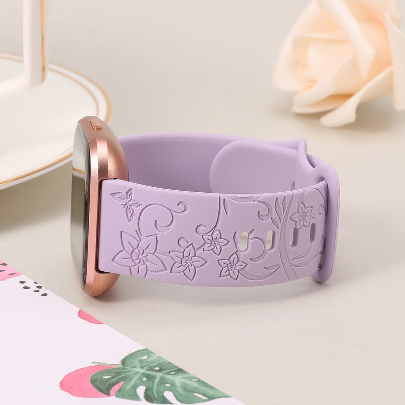 May include: A lavender silicone watch band with a floral design. The band is compatible with smartwatches with a 20mm band size.
