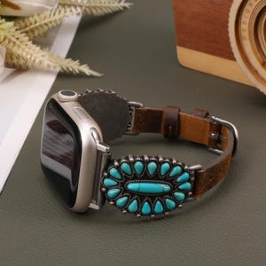 Puede incluir: Una correa de Apple Watch de cuero marrón con una hebilla decorativa turquesa y plateada. La correa está diseñada con un estilo del suroeste.