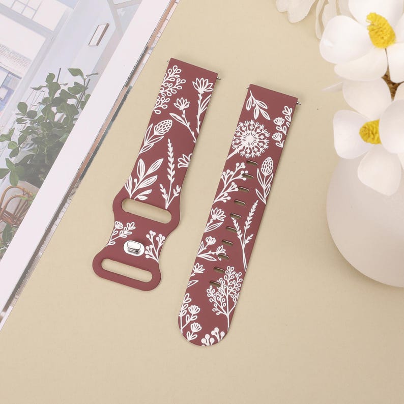 May include: Two red silicone watch bands with a white floral pattern. The bands have a buckle closure and are designed for smartwatches.