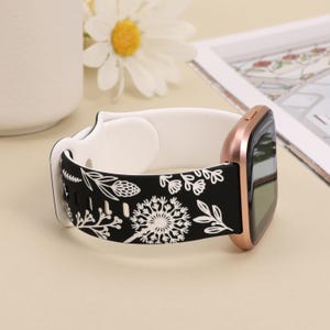 May include: Black and white floral patterned watch band with a rose gold watch face. The band is made of silicone and has a white buckle.