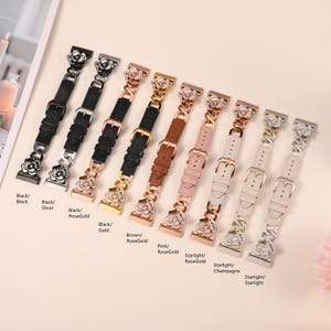 May include: A collection of watch bands in various colors, including black, silver, rose gold, brown, and pink. Each band features a decorative floral accent and a buckle closure. The bands are displayed on a light-colored surface.