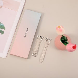 Puede incluir: Dos correas de reloj de cuero beige claro con cierres y hebillas plateadas. Las correas est&aacute;n dispuestas sobre una caja de degradado rosa claro y azul que dice "Watch Band".