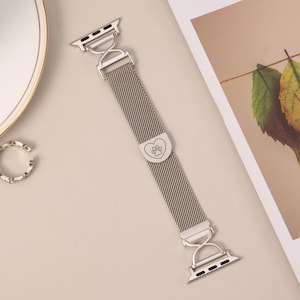 以下が含まれることがあります： ハート型のチャームに肉球の刻印が施された、シルバーメタルのApple Watchバンド。メッシュデザインで留め具付きです。