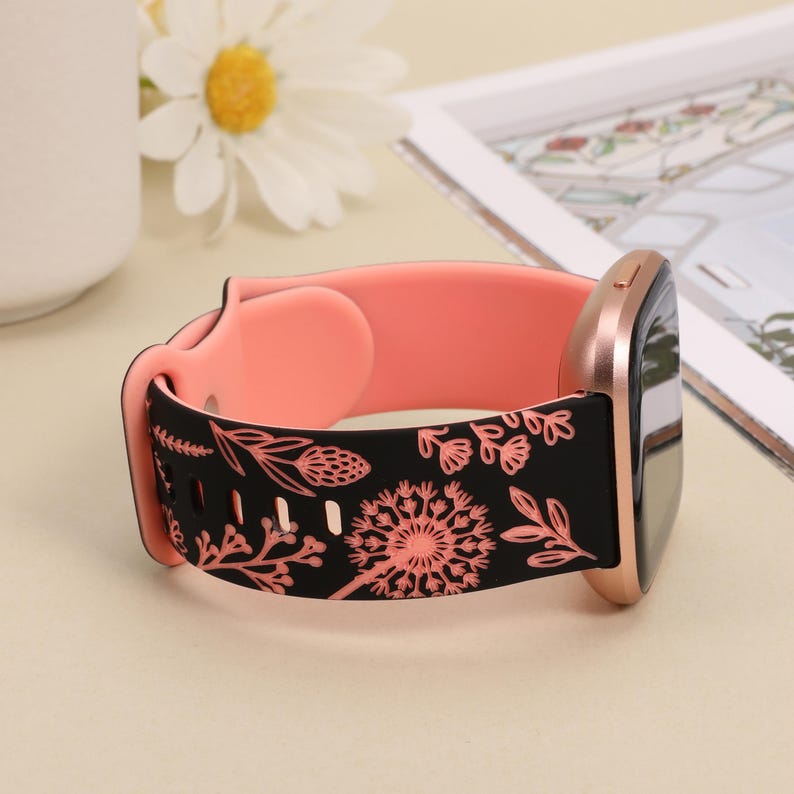 May include: A black and pink silicone watch band with a floral pattern. The band is designed for a smartwatch with a square face.