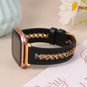 May include: A rose gold smartwatch with a black leather band featuring a gold chain design. The watch has a rectangular screen and a gold buckle. The band is connected to the watch with gold hardware.