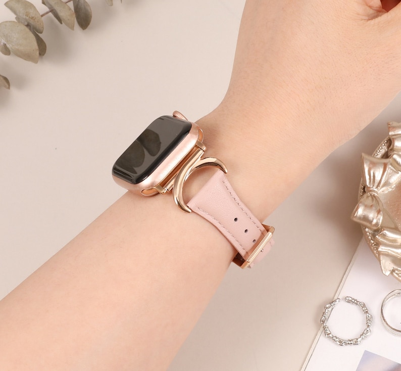 Puede incluir: Una correa de Apple Watch de oro rosa con un dise&ntilde;o de media luna. La correa est&aacute; hecha de cuero y tiene una hebilla de oro rosa.