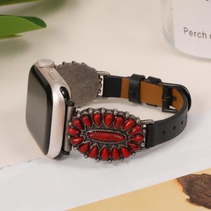 Op de afbeelding: Zwart leren Apple Watch-band met een rode en zilveren sierlijke gesp. De gesp heeft een rood stenen ontwerp.