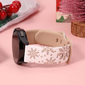 May include: White silicone watch band with a snowflake pattern in gold. The band is compatible with smartwatches.