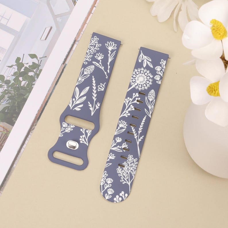May include: Two blue silicone watch bands with a white floral pattern. The bands are designed for smartwatches.