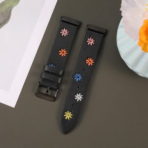 Puede incluir: Dos correas de reloj de cuero negro con flores bordadas de colores. Las correas tienen un cierre de hebilla.