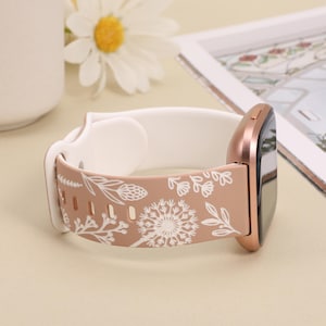 May include: A rose gold silicone watch band with a white floral pattern. The band is designed for a smartwatch with a square face.