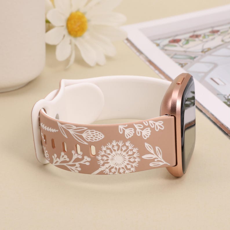 May include: A rose gold silicone watch band with a white floral pattern. The band is designed for a smartwatch with a square face.