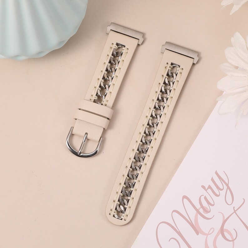May include: Cream-colored watch band with a silver chain design. The band features a silver buckle and a chain that runs down the center. The watch band is made of a soft material and is displayed on a light pink surface.