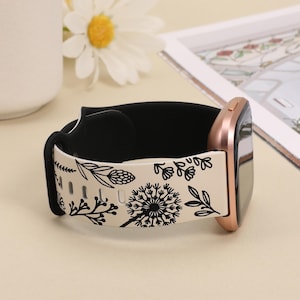 May include: A white and black floral patterned watch band with a rose gold watch face. The band is made of silicone and has a black inner layer.
