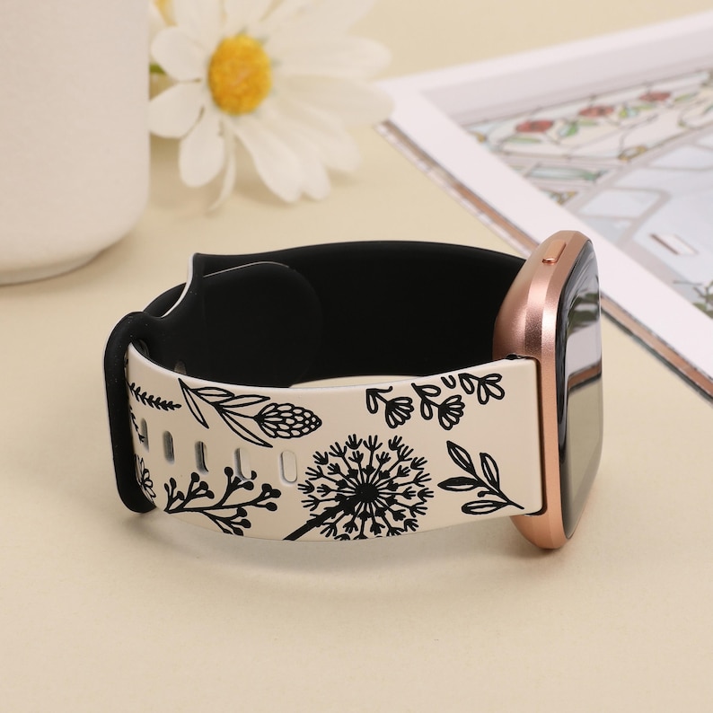 May include: A white and black floral patterned watch band with a rose gold watch face. The band is made of silicone and has a black inner layer.