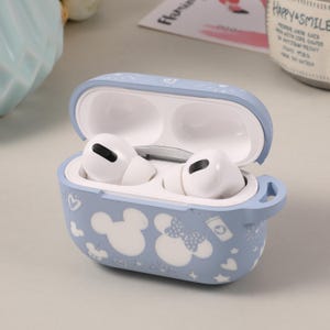 May include: A light blue silicone case for AirPods with a Mickey Mouse and Minnie Mouse design. The case has a small loop on the side for attaching a strap.