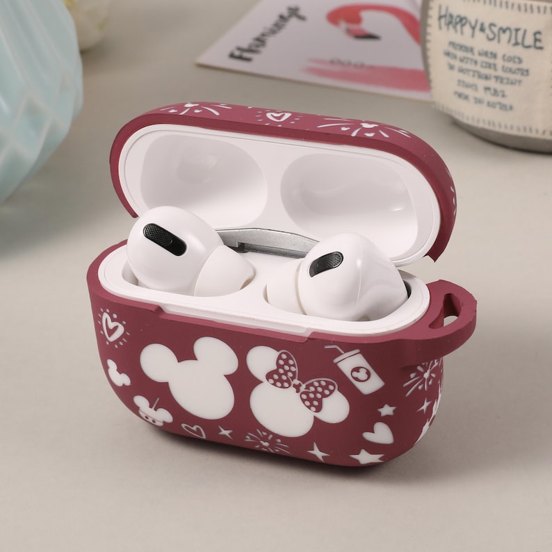 May include: A burgundy silicone case for wireless earbuds with a white Mickey Mouse and Minnie Mouse design. The case has a white outline of hearts, stars, and other doodles. The case is open and the earbuds are inside.