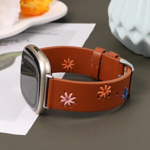 Puede incluir: Una correa de reloj de cuero marr&oacute;n con un dise&ntilde;o de bordado floral. La correa tiene una hebilla plateada y es compatible con los relojes inteligentes.