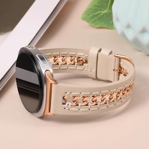 以下が含まれることがあります： 黒い画面とクリーム色の革バンドが付いたシルバーのスマートウォッチ。バンドは、革に縫い付けられたゴールドチェーンのデザインが特徴です。時計にはゴールドのアクセントとゴールドのバックルが付いています。