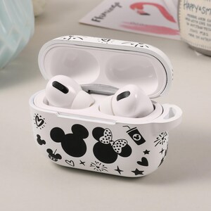 May include: White protective case for wireless earbuds with a black and white design featuring Mickey Mouse and Minnie Mouse. The case has a hinged lid and a small loop on the side.