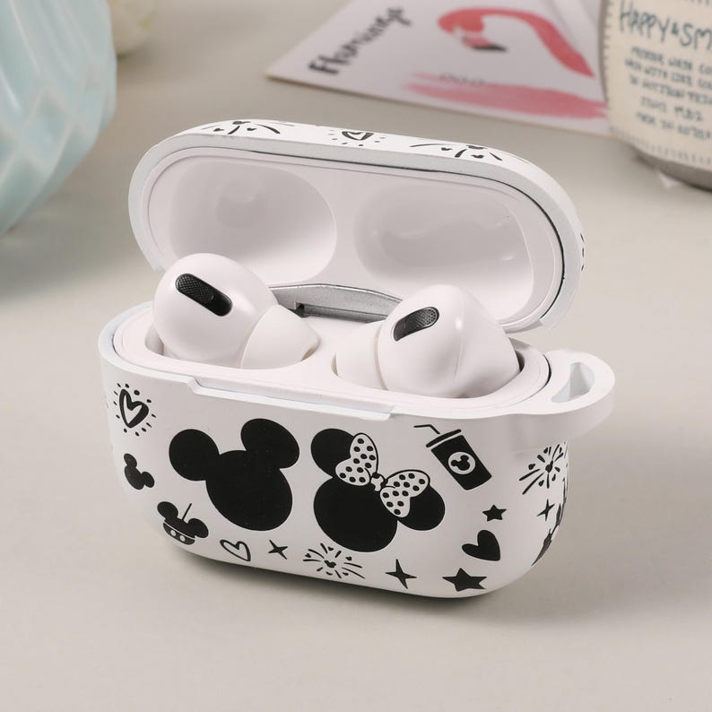 May include: White protective case for wireless earbuds with a black and white design featuring Mickey Mouse and Minnie Mouse. The case has a hinged lid and a small loop on the side.
