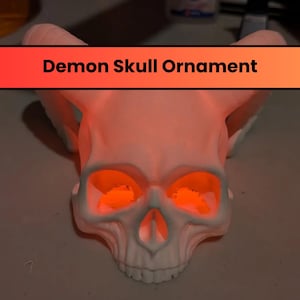 Puede incluir: Adorno de calavera de demonio blanco con ojos naranja brillantes. La calavera tiene cuernos y una cara detallada.