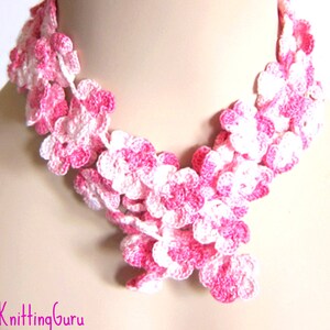 Puede incluir: Un collar de flores de ganchillo rosa y blanco. El collar está hecho de pequeñas flores delicadas que están conectadas entre sí para formar una cadena continua. Las flores son una mezcla de rosa y blanco, y están dispuestas en un patrón aleatorio.