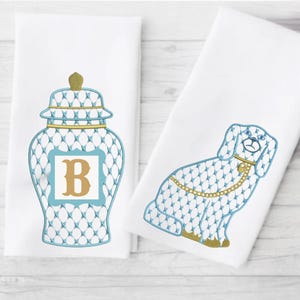 May include: Two white kitchen towels with blue and gold embroidery. One towel features a blue and gold ginger jar with the letter "B" in the center. The other towel features a blue and gold dog.