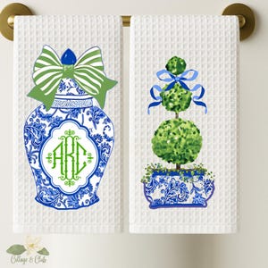 May include: Two white kitchen towels with blue and white patterned designs. One towel features a blue and white ginger jar with a green bow and monogram "ARC". The other towel features a blue and white planter with a green topiary tree and a blue bow.