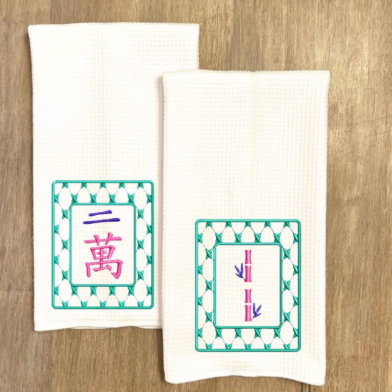 May include: Two white kitchen towels with embroidered Chinese characters and bamboo designs. The first towel has a green square frame with the Chinese character for "three" and the word "bamboo" in a smaller square inside. The second towel has a green square frame with a stylized image of two bamboo stalks with leaves.