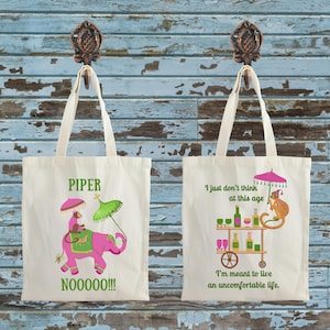 May include: Two white canvas tote bags with different designs. The left bag has a pink elephant with a monkey riding on top and the text "PIPER NOOOOO!!!". The right bag has a monkey sitting on a bar cart with drinks and the text "I just don't think at this age I'm meant to live an uncomfortable life."