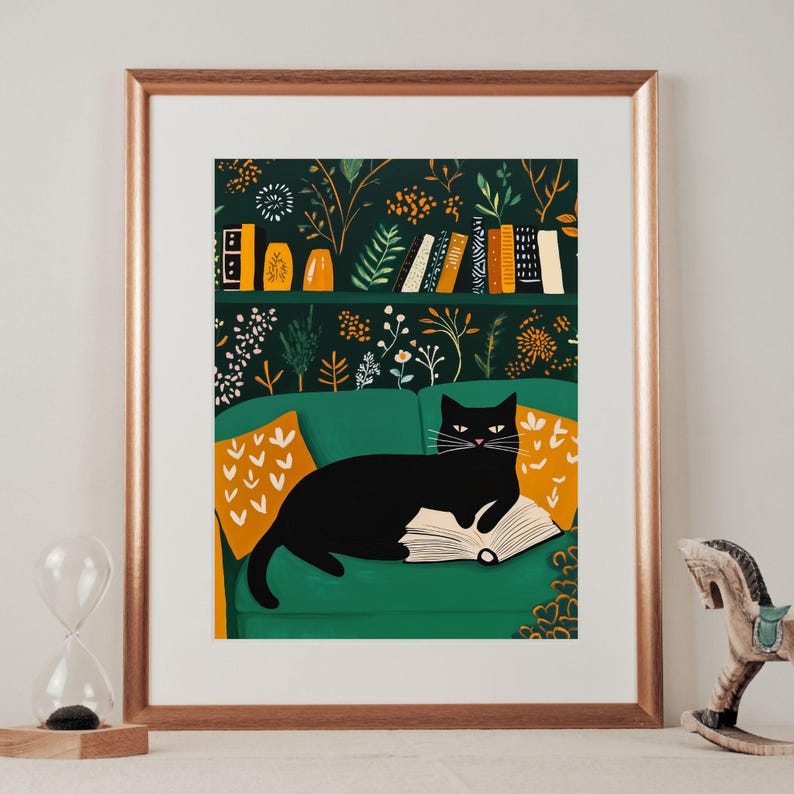 May include: A framed art print featuring a black cat lounging on a green sofa, reading a book. The background showcases a bookshelf with books and decorative items, set against a dark green floral wallpaper. Orange and yellow throw pillows add color.