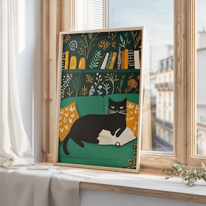 May include: A framed art print featuring a black cat lounging on a green sofa, reading a book. The background includes a bookshelf with books and floral wallpaper. Yellow pillows with arrow patterns add color.