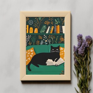 May include: A framed art print featuring a black cat lounging on a green sofa, reading a book. The background includes a bookshelf and floral wallpaper. The print is in a light-colored wooden frame, with lavender sprigs in the foreground.