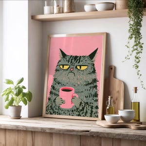 Puede incluir: Una lámina de arte enmarcada que muestra a un gato atigrado gris y gruñón con ojos amarillos sosteniendo una taza de café rosa sobre un fondo rosa sólido. El gato tiene un pelaje oscuro y texturizado con una expresión facial severa en un marco de madera.