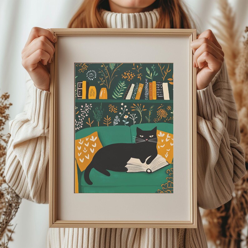 May include: A framed art print featuring a black cat lounging on a green sofa with a book. The background shows a bookshelf and floral wallpaper. Yellow pillows add color to the scene. The frame is a light wood color.