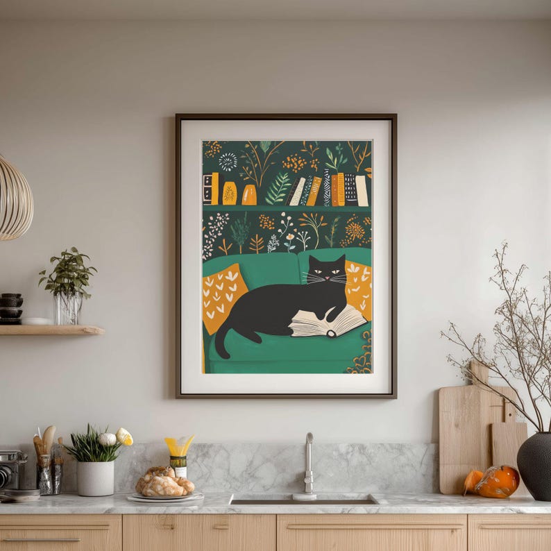 May include: Framed art print featuring a black cat lounging on a green sofa, reading a book. The background includes a bookshelf with books and decorative items. The sofa has yellow patterned pillows. The artwork is framed in a dark brown frame.